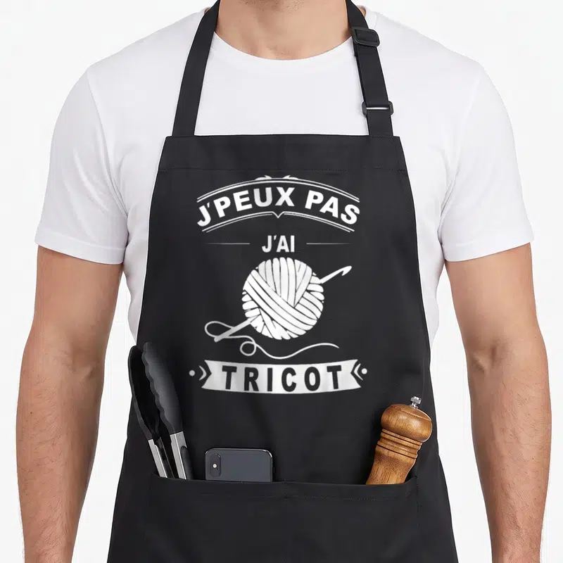 Tablier de cuisine noir avec un ballon de laine, une aiguille et le texte J'peux pas j'ai tricot imprimé en blanc.