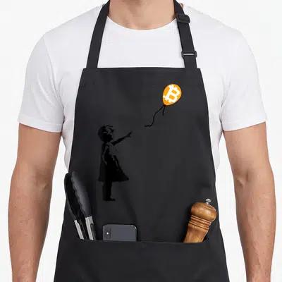 Tablier de cuisine noir avec silhouette enfant pointant vers un ballon orange au logo Bitcoin blanc.