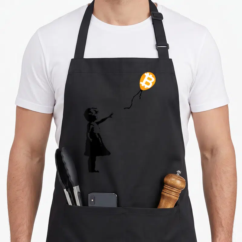 Tablier de cuisine noir avec silhouette enfant pointant vers un ballon orange au logo Bitcoin blanc.