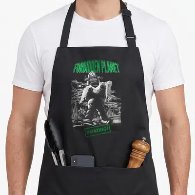 Tablier de cuisine noir avec illustration retro d'un robot géant portant une femme sous le titre Forbidden Planet en vert.