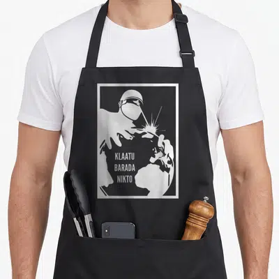 Tablier de cuisine noir avec illustration robot soudant une carte du monde et le texte Klaatu Barada Nikto en blanc.