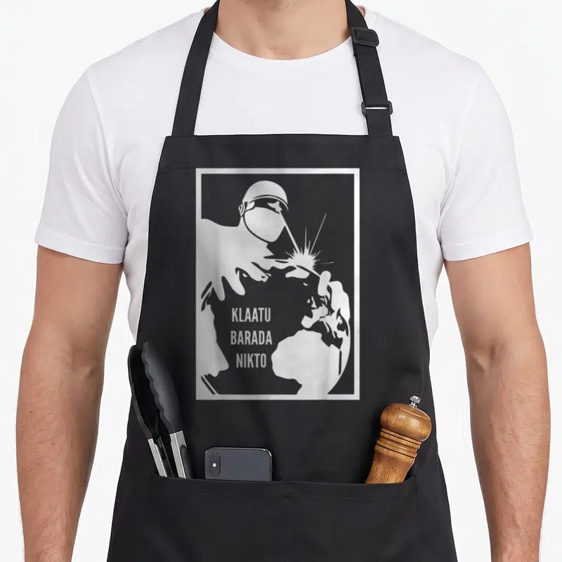 Tablier de cuisine noir avec illustration robot soudant une carte du monde et le texte Klaatu Barada Nikto en blanc.