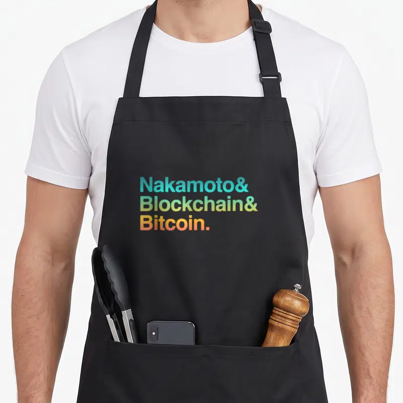 Tablier de cuisine noir avec le texte Nakamoto Blockchain Bitcoin en lettres colorées sur fond uni.