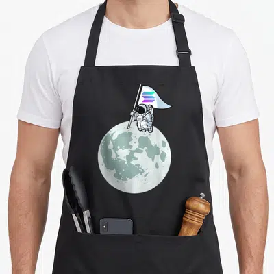Tablier de cuisine noir avec illustration d'un astronaute plantant un drapeau aux trois bandes colorées sur une surface lunaire.