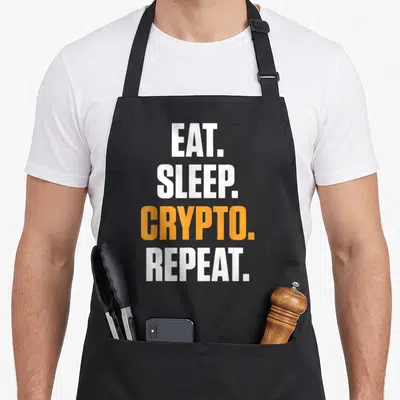 Tablier de cuisine noir avec le texte blanc et orange Eat Sleep Crypto Repeat imprimé au centre.