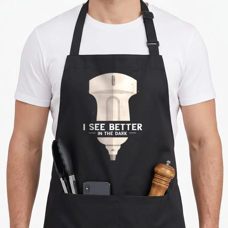Tablier de cuisine noir avec échographe beige et texte blanc « I see better in the dark »