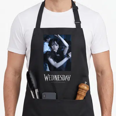 Tablier de cuisine noir avec une scène de danse et le nom WEDNESDAY imprimé en bas.