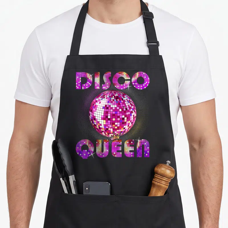 Tablier de cuisine noir avec une boule miroir rose et le texte Disco Queen en lettres pixelisées colorées.