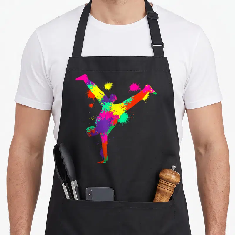 Tablier de cuisine noir avec silhouette multicolore d'un breakdancer effectuant un mouvement acrobatique et des éclaboussures artistiques.