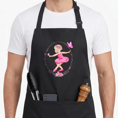Tablier de cuisine noir avec une ballerine en tutu rose entourée de roses et de papillons dans un cadre ovale.