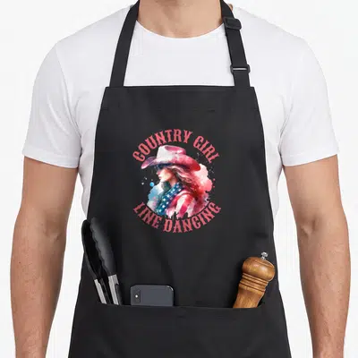 Tablier de cuisine noir avec une femme au chapeau cowboy et le texte Country Girl Line Dancing en aquarelle.