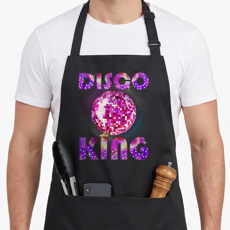 Tablier de cuisine noir avec un miroir disco rose et l'inscription Disco King en lettres pixelisées multicolores.