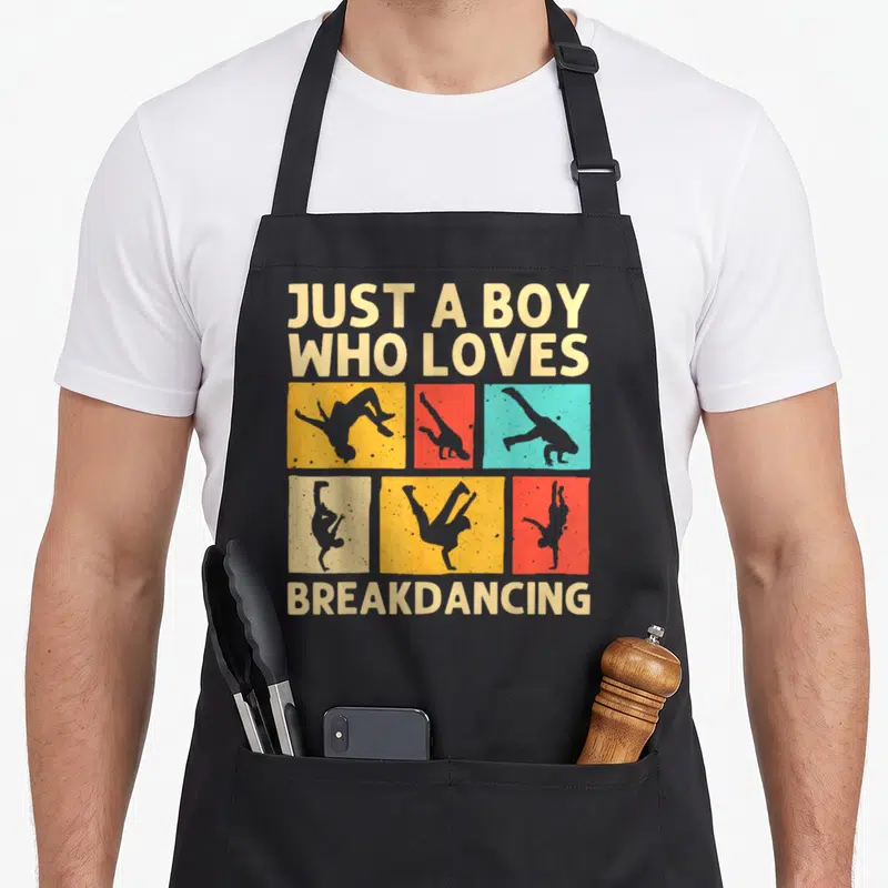 Tablier de cuisine noir avec silhouettes de danseurs et texte Just a boy who loves breakdancing en lettres claires.