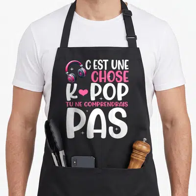 Tablier de cuisine noir avec des écouteurs roses et le texte C'est une chose K-pop tu ne comprendrais pas imprimé en blanc et rose.