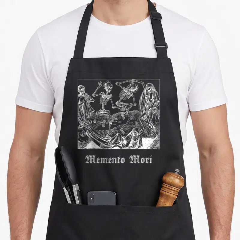 Tablier de cuisine noir avec illustration blanche de squelettes dansant et texte Memento Mori en bas.