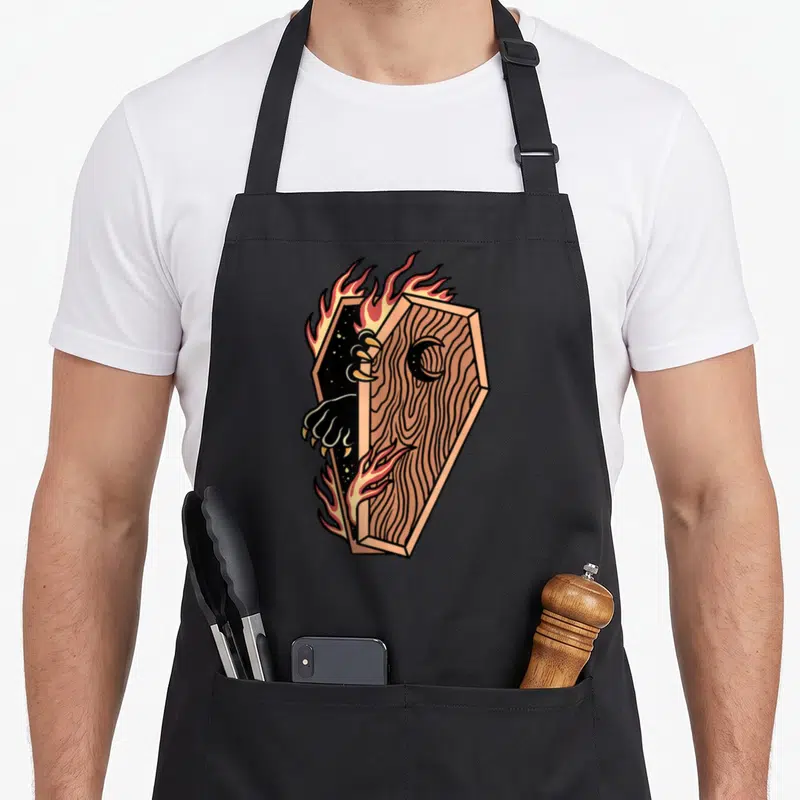 Tablier de cuisine noir avec illustration d'un cercueil enflammé aux griffes noires sortant de l'ombre.
