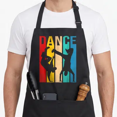 Tablier de cuisine noir avec inscription DANCE et silhouettes de danseurs de hip-hop sur bandes colorées verticales.