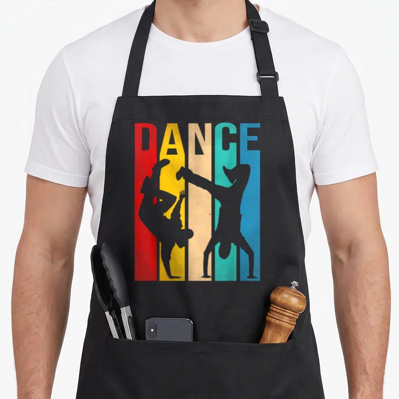 Tablier de cuisine noir avec inscription DANCE et silhouettes de danseurs de hip-hop sur bandes colorées verticales.