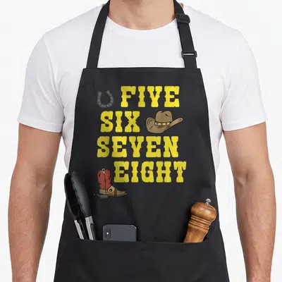 Tablier de cuisine noir avec inscription Five Six Seven Eight, chapeau cowboy, bottine rouge et fer à cheval jaune.