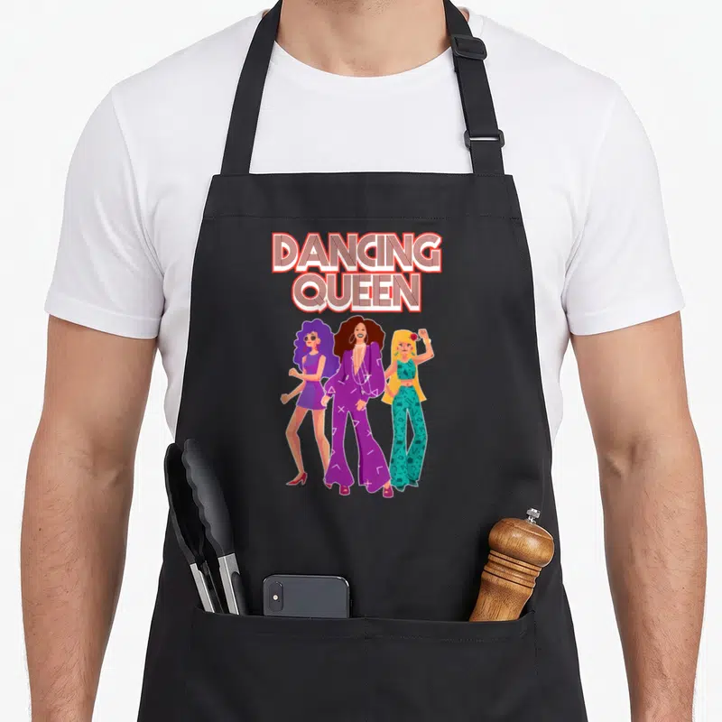 Tablier de cuisine noir avec trois femmes stylisées en tenues disco et l'inscription Dancing Queen en lettres rétro.