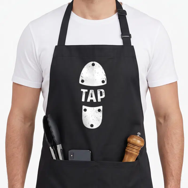 Tablier de cuisine noir avec illustration blanche de plaque de tap et linscription TAP au centre.