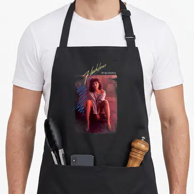 Tablier de cuisine noir avec une illustration d'une femme assise et le texte Flashdance What a feeling en typographie stylisée.