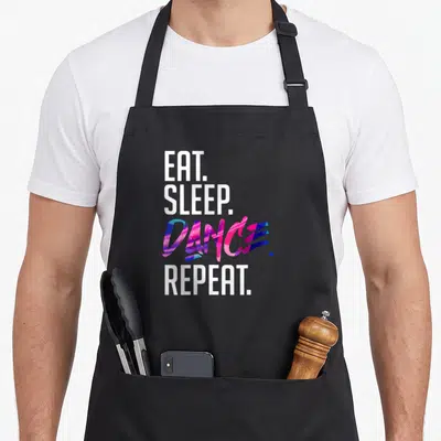 Tablier de cuisine noir avec le texte Eat Sleep Dance Repeat en typographie blanche et colorée sur fond uni.