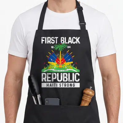 Tablier de cuisine noir avec le drapeau haïtien, palmier, canons et texte First Black Republic Haiti Strong imprimé au centre.