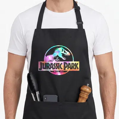 Tablier de cuisine noir avec le logo Jurassic Park rempli de motifs tie dye multicolores vifs.