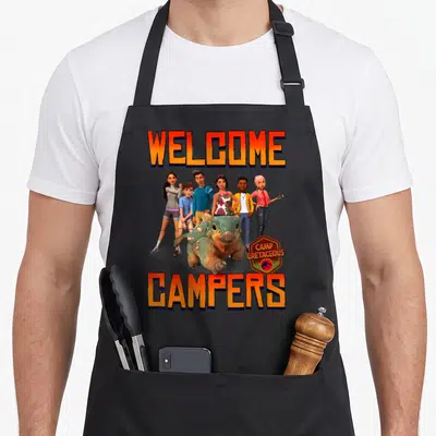 Tablier de cuisine noir avec le groupe Welcome Campers, un dinosaure vert et le logo Camp Cretaceous en bas à droite.