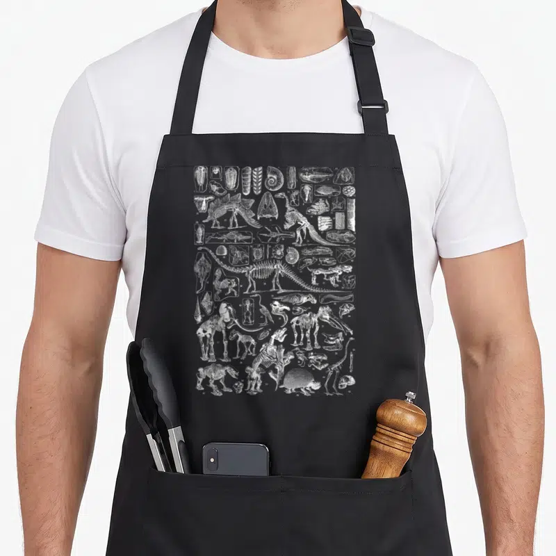 Tablier de cuisine noir avec illustration blanche détaillée de fossiles et squelettes de dinosaures vintage.
