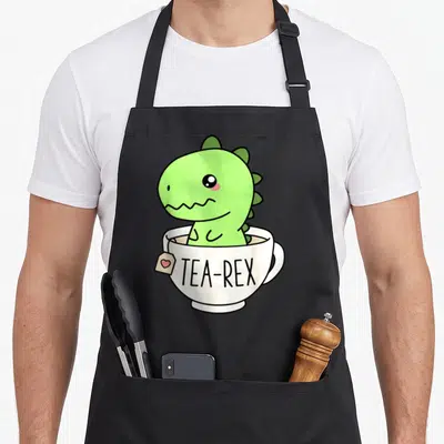 Tablier de cuisine noir avec un dinosaure vert kawaii assis dans une tasse blanche portant l'inscription Tea-Rex.