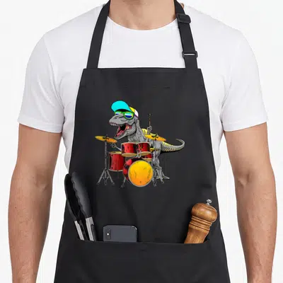 Tablier de cuisine noir avec illustration d'un T rex batteur portant une casquette et des lunettes de soleil devant une batterie rouge.