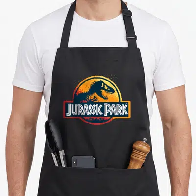Tablier de cuisine noir avec logo Jurassic Park en pixel art coloré et style rétro.