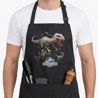 Tablier de cuisine noir avec illustration d'un grand dinosaure blanc entouré de petits raptors verts et du logo Jurassic World.