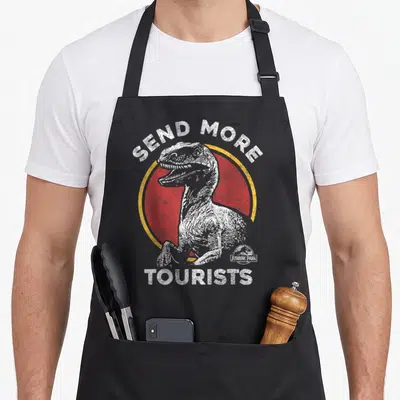 Tablier de cuisine noir avec illustration de raptor blanc sur fond rouge et texte Send More Tourists en haut et en bas.