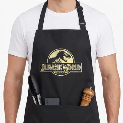 Tablier de cuisine noir avec le logo Jurassic World imprimé en doré texturé sur le devant.