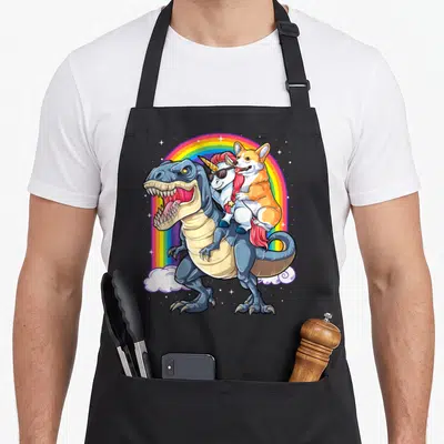 Tablier de cuisine noir avec illustration d'un dinosaure portant un corgi et une licorne devant un arc-en-ciel.