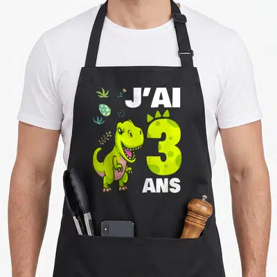 Tablier de cuisine noir avec illustration d'un dinosaure vert et l'inscription J'ai 3 ans en lettres blanches et jaunes.