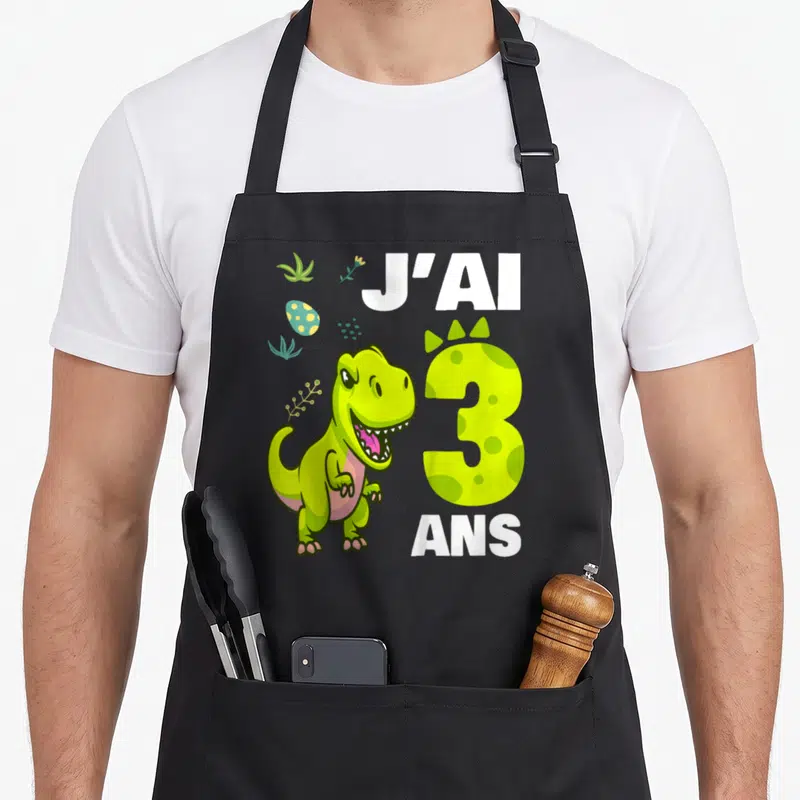 Tablier de cuisine noir avec illustration d'un dinosaure vert et l'inscription J'ai 3 ans en lettres blanches et jaunes.