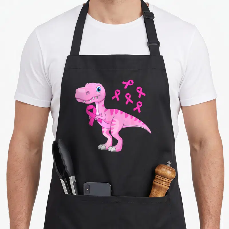 Tablier de cuisine noir avec illustration d'un dinosaure rose tenant un ruban et des symboles de sensibilisation.