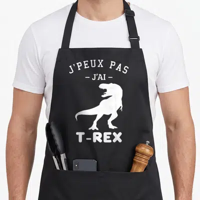 Tablier de cuisine noir avec silhouette blanche de T-Rex et texte J'peux pas j'ai T-Rex en haut.