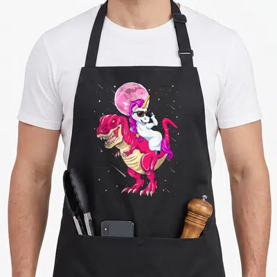 Tablier de cuisine noir avec illustration d'un dinosaure rose portant une licorne aux lunettes noires sous une lune rose.