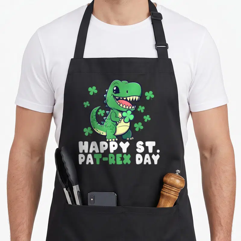 Tablier de cuisine noir avec un crocodile vert tenant un trèfle et le texte Happy St Pat-Rex Day