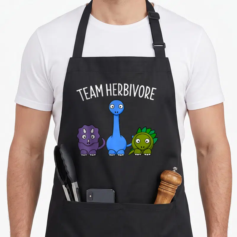 Tablier de cuisine noir avec trois dinosaures colorés et l'inscription Team Herbivore en blanc.