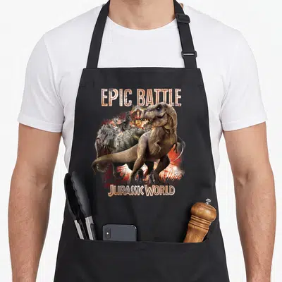Tablier de cuisine noir avec illustration de deux dinosaures prédateurs en combat et texte Epic Battle Jurassic World.