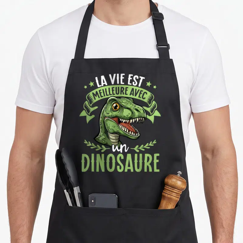 Tablier de cuisine noir avec illustration d'un dinosaure vert et le texte la vie est meilleure avec un dinosaure