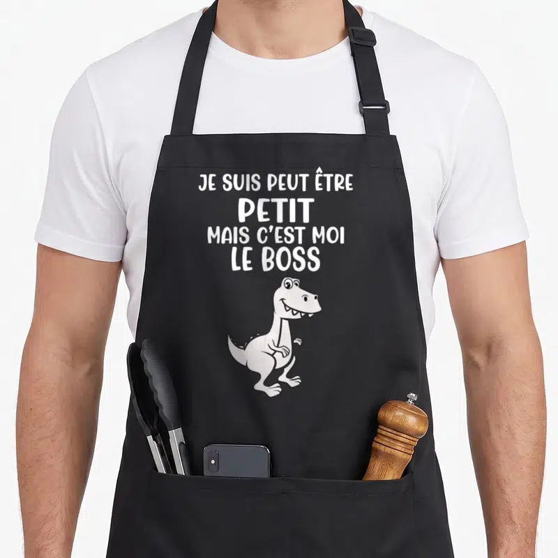 Tablier de cuisine noir avec un dessin de T-Rex blanc et le texte Je suis petit mais c'est moi le boss imprimé en haut.