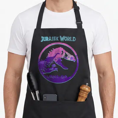 Tablier de cuisine noir avec illustration colorée d'un crâne de dinosaure dans un cercle rose et violet, surmonté du texte Jurassic World en bleu clair.