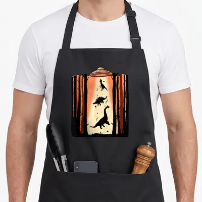 Tablier de cuisine noir avec illustration d'un ovin capturant des dinosaures dans une forêt orange.